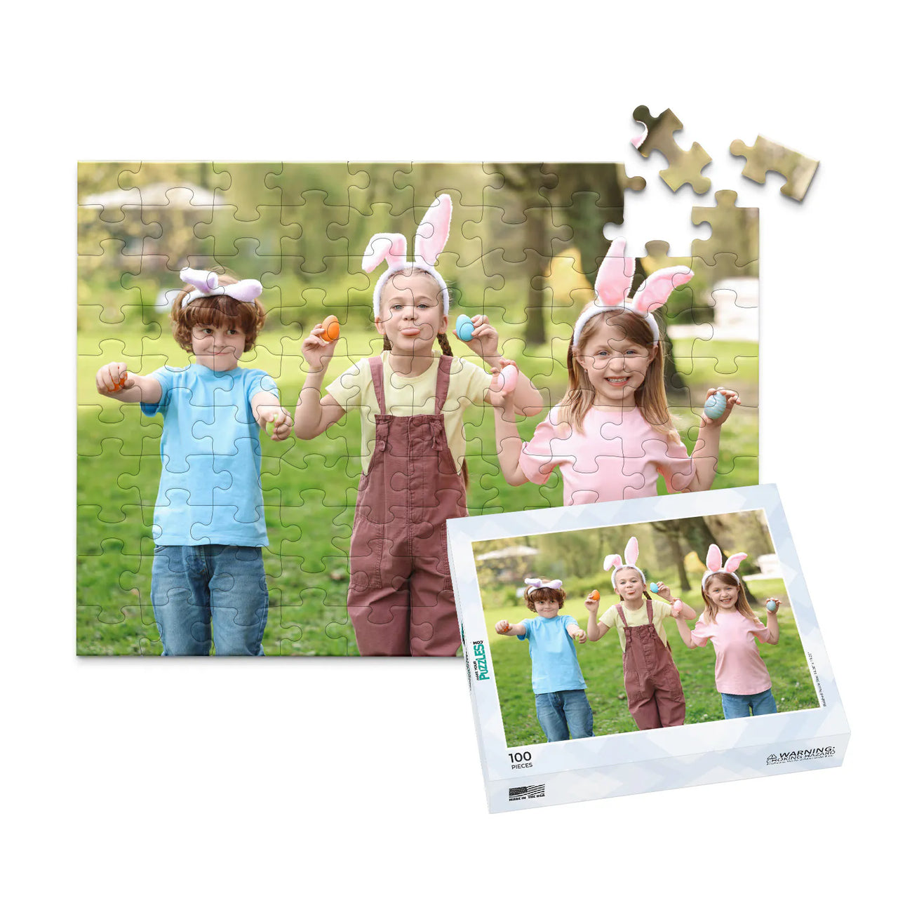 100 piece Easter photo puzzle featuring three children wearing bunny ears and holding colorful Easter eggs, shown with its matching puzzle box