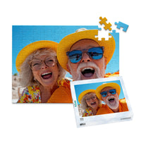 100 piece personalized couple puzzle featuring a joyful older couple wearing sun hats at the beach, shown with its matching puzzle box