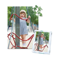 100 piece personalized puzzle for kids showing a smiling young girl climbing playground ropes, displayed with the matching puzzle box.
