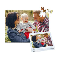 100 piece personalized puzzle for new parents showing a smiling mother and father holding their baby outdoors, displayed with the matching puzzle box.