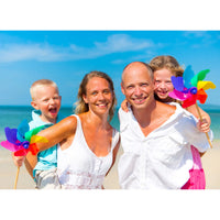 Custom Travel Photo Puzzle landscape orientation of a family of four smiling on a sunny beach, each holding a colorful rainbow pinwheel. The mother is wearing a white tank top, the father is in a white button-down shirt, and the children are dressed in light summer clothing.