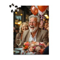 Personalized Birthday Puzzle 500 Pieces featuring a photo of a smiling older man with a white beard and glasses, wearing a brown blazer, seated at a table with balloons, flowers, and a champagne flute.