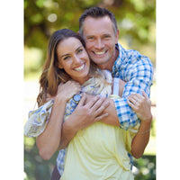 Personalized Couple Puzzle showing a smiling couple embracing outdoors, with the man wearing a blue and white checkered shirt and the woman in a pale yellow top. The background is a soft, blurred green natural setting.